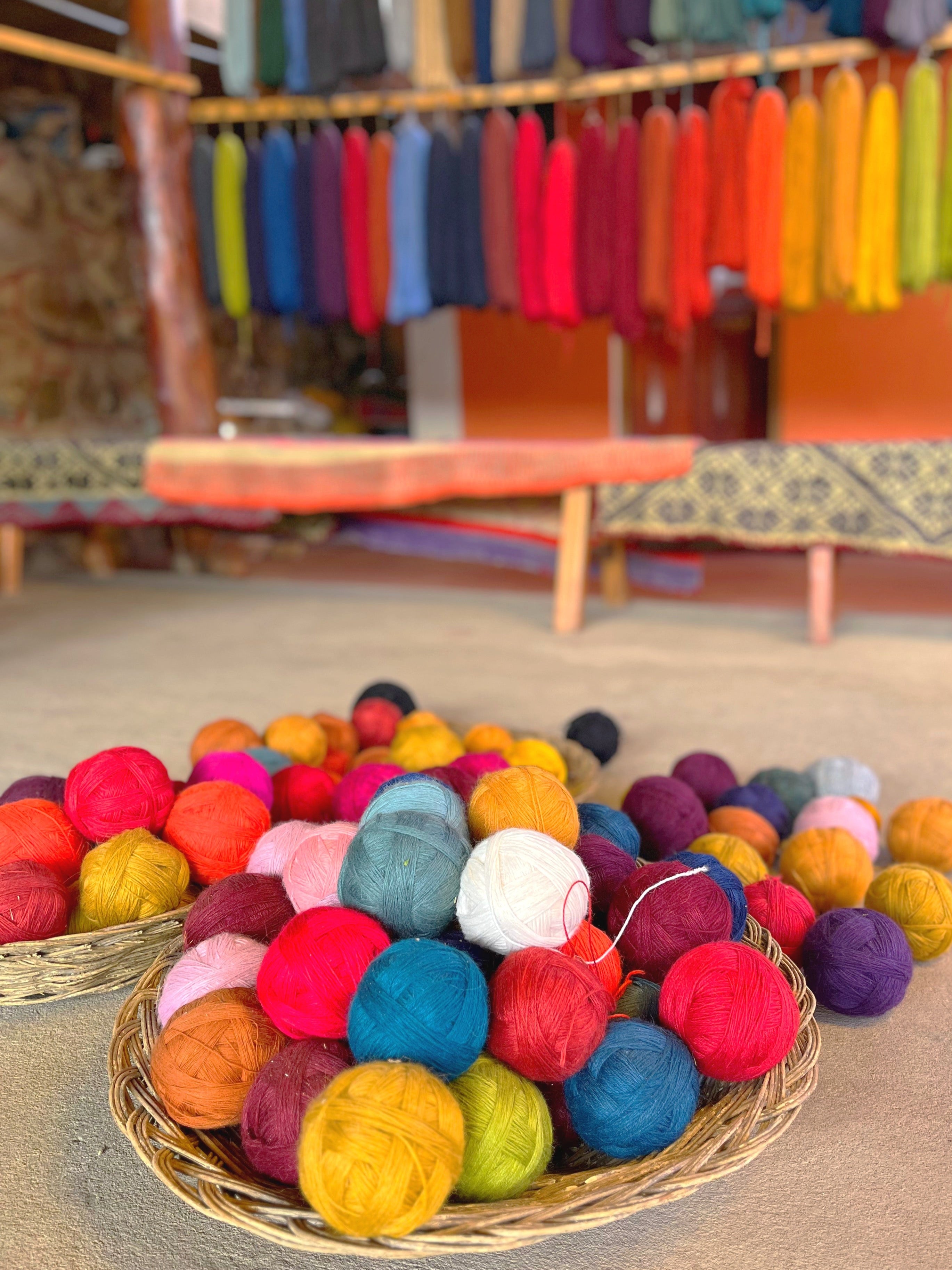 Colorful yarn balls in a basket with a blurred background of fabric racks.