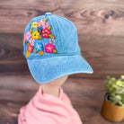 Blue denim cap with floral embroidery on a wooden surface.